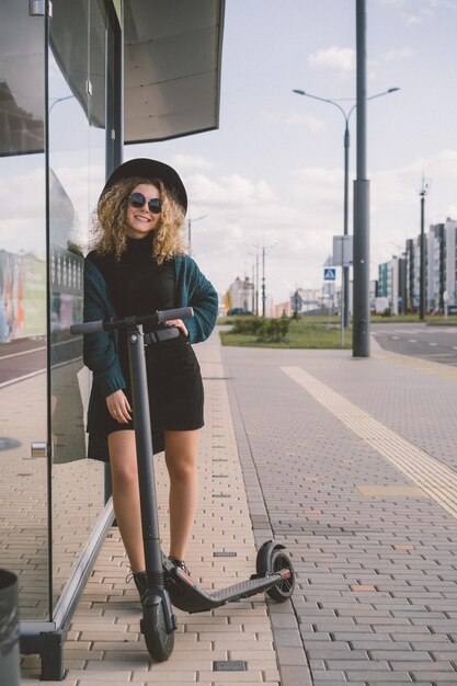 Mujer hermosa joven montando un scooter eléctrico para trabajar, chica moderna, nueva generación, transporte eléctrico, ecología, transporte ecológico, puesta de sol