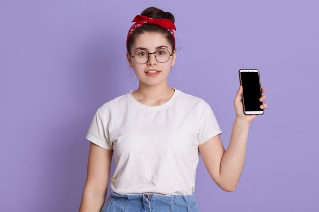 Mujer hermosa joven muestra a la derecha en la pantalla en blanco de la cámara del teléfono inteligente aislado sobre el espacio lila