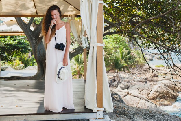 Mujer hermosa joven natural en vestido pálido posando en marquesina, vacaciones tropicales,