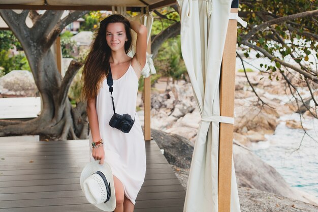 Mujer hermosa joven natural en vestido pálido posando en marquesina, vacaciones tropicales,