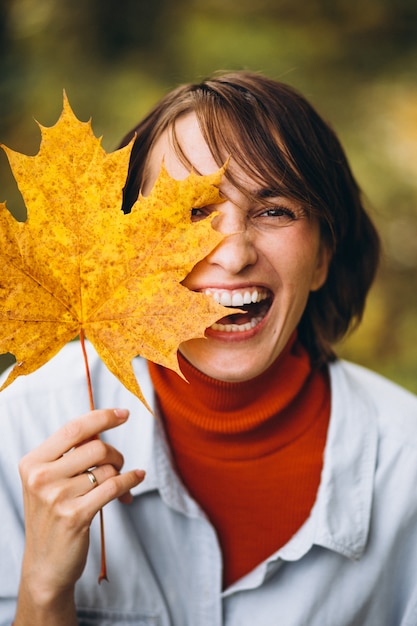 Mujer hermosa joven en un parque de otoño lleno de hojas