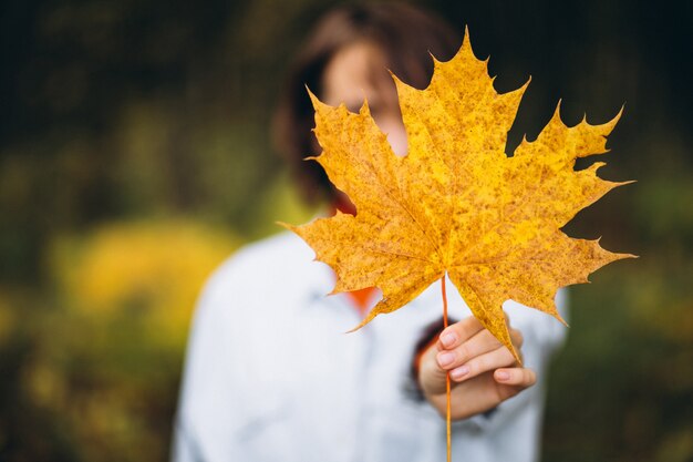 Mujer hermosa joven en un parque de otoño lleno de hojas