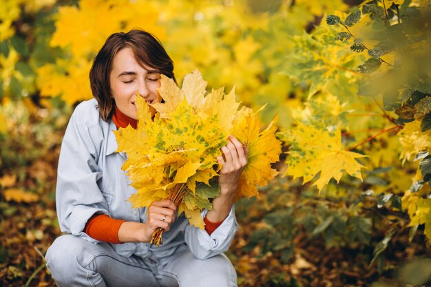 Mujer hermosa joven en un parque de otoño lleno de hojas