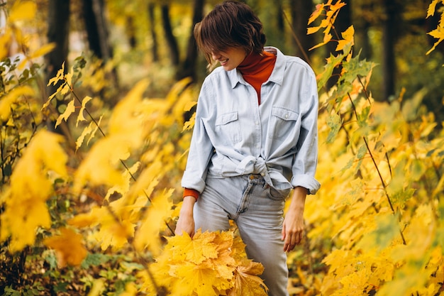 Mujer hermosa joven en un parque de otoño lleno de hojas