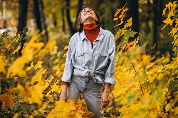 Mujer hermosa joven en un parque de otoño lleno de hojas