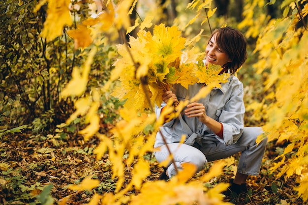 Mujer hermosa joven en un parque de otoño lleno de hojas