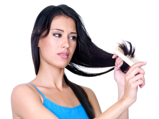 Mujer hermosa joven peinándose y mirando las puntas del cabello - aislado