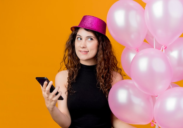 Mujer hermosa joven con el pelo rizado en un sombrero de fiesta con montón de globos de aire