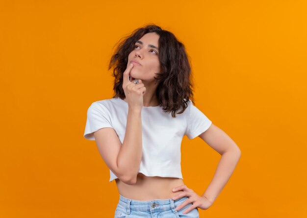 Mujer hermosa joven pensativa poniendo el dedo en el labio en la pared naranja aislada con espacio de copia