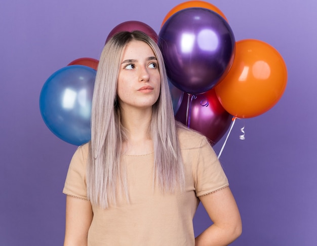 Mujer hermosa joven de pie delante de globos aislados en la pared azul