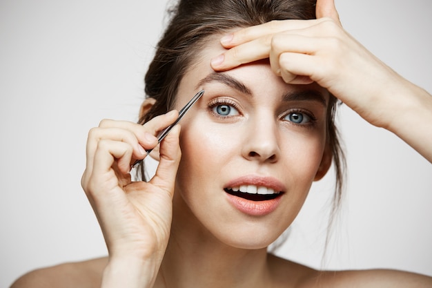 La mujer hermosa joven con la piel limpia perfecta depila las cejas. Tratamiento facial.