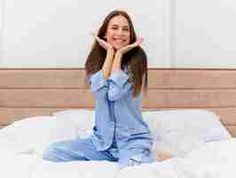 Foto gratuita mujer hermosa joven en pijama azul sentada en la cama descansando feliz y positivo sonriendo disfrutando de fin de semana en el interior del dormitorio