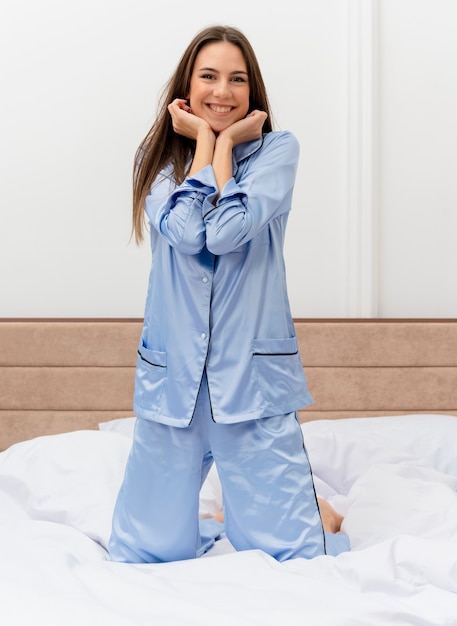 Mujer hermosa joven en pijama azul sentado en la cama descansando disfrutando de fin de semana feliz y positivo sonriendo alegremente en el interior del dormitorio