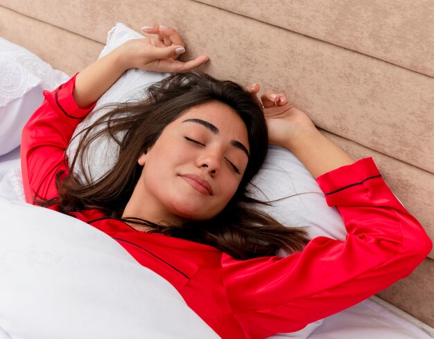 Mujer hermosa joven en pijama rojo relajante en la cama