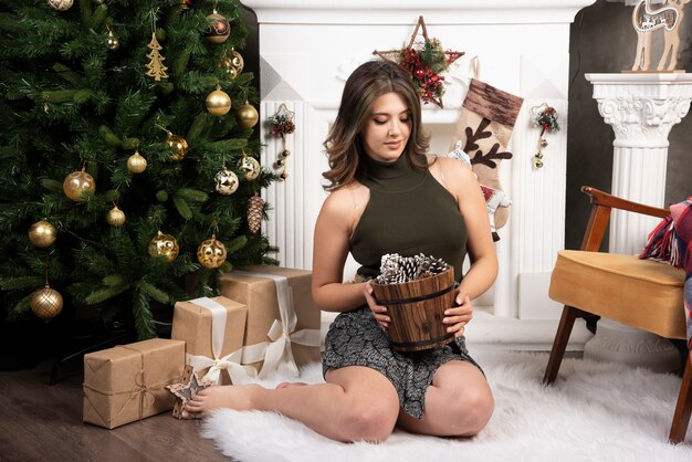 Mujer hermosa joven posando con canasta de piñas cerca del árbol de Navidad