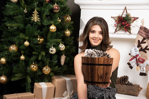 Mujer hermosa joven posando con canasta de piñas cerca del árbol de Navidad