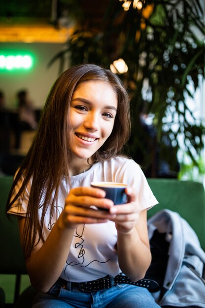 Mujer hermosa joven que bebe capucino en café