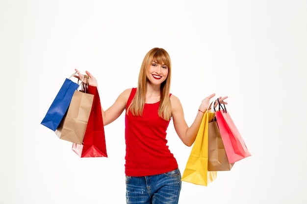 Mujer hermosa joven que se coloca con las compras sobre la pared blanca