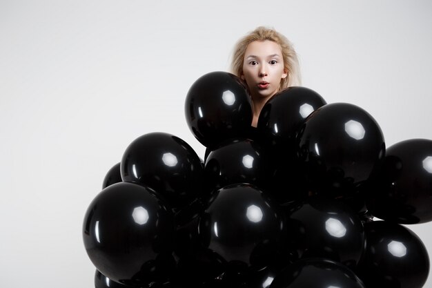 Mujer hermosa joven que se coloca en globos negros sobre la pared blanca