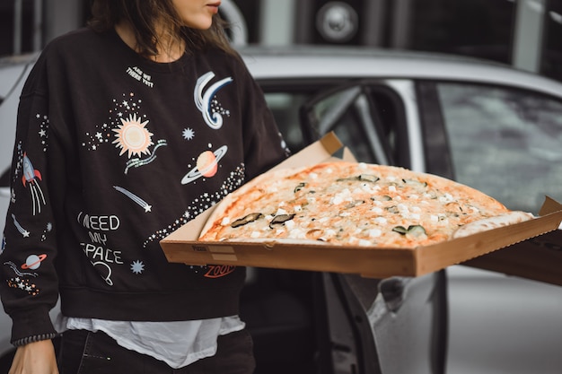 Mujer hermosa joven que come una rebanada de pizza en la calle de la ciudad