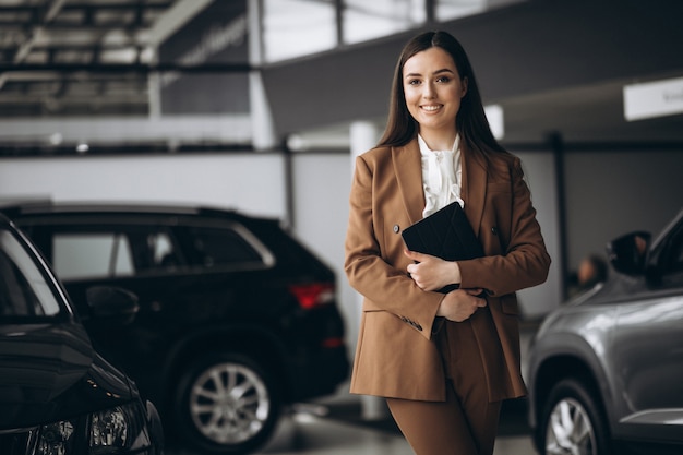 Mujer hermosa joven que elige el coche en una sala de exposición de automóviles