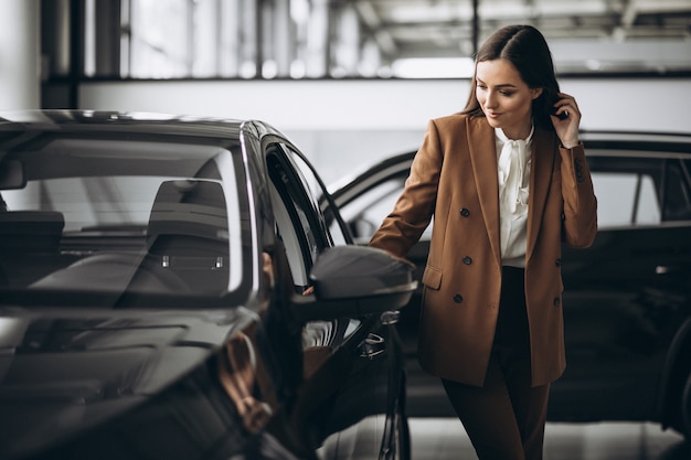 Mujer hermosa joven que elige el coche en una sala de exposición de automóviles