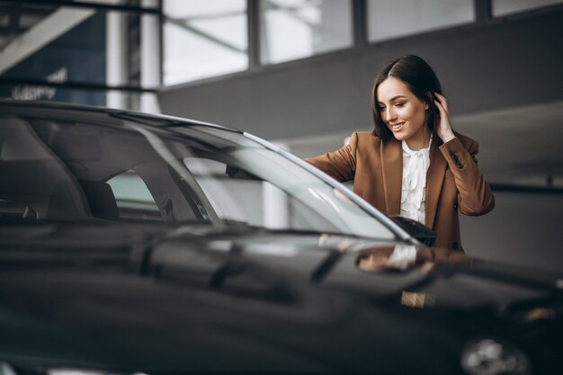 Mujer hermosa joven que elige el coche en una sala de exposición de automóviles