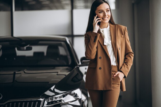 Mujer hermosa joven que elige el coche en una sala de exposición de automóviles