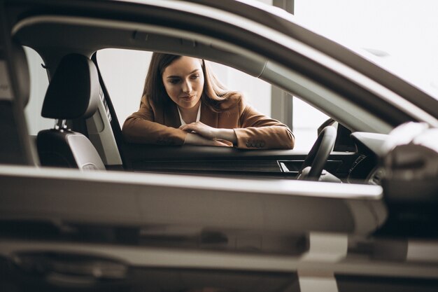 Mujer hermosa joven que elige el coche en una sala de exposición de automóviles