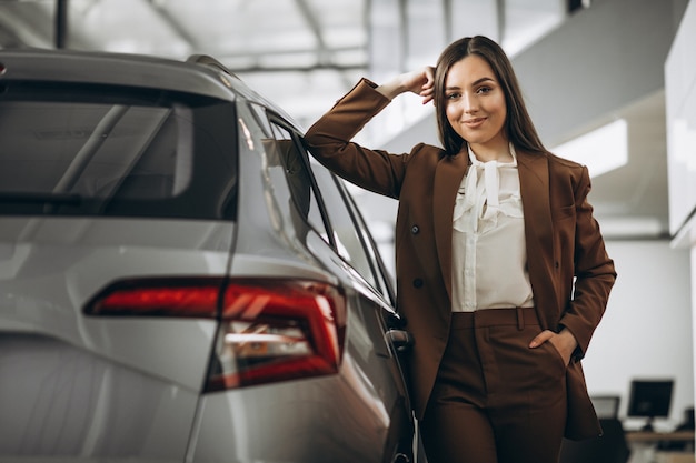 Mujer hermosa joven que elige el coche en una sala de exposición de automóviles
