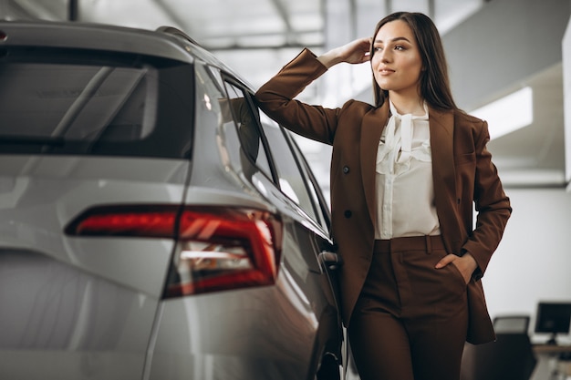 Mujer hermosa joven que elige el coche en una sala de exposición de automóviles