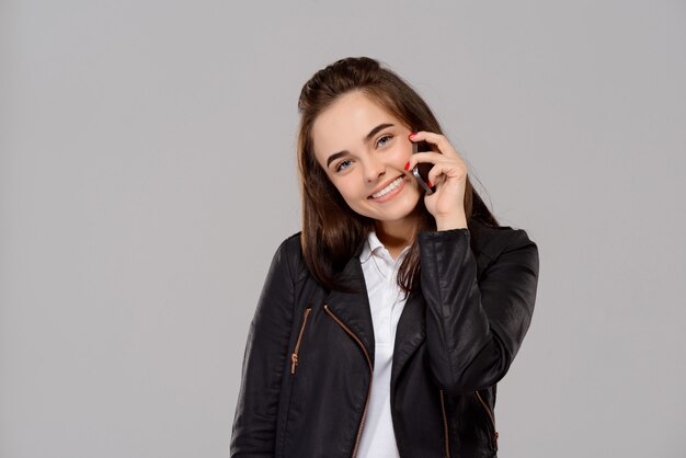 Mujer hermosa joven que habla en el teléfono, sonriendo sobre la pared púrpura