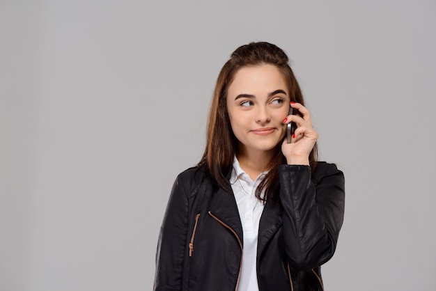 Mujer hermosa joven que habla en el teléfono, sonriendo sobre la pared púrpura