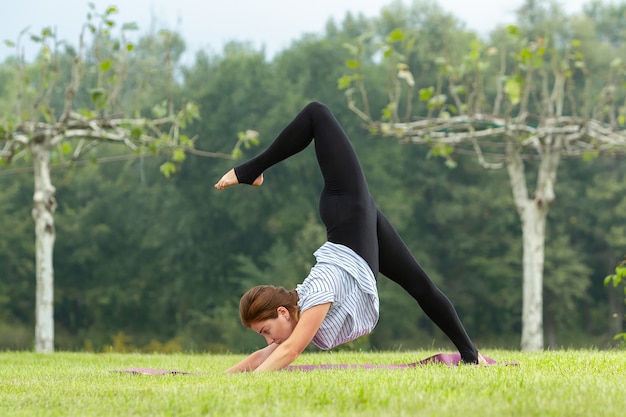 Mujer hermosa joven que hace ejercicio de yoga en el parque verde cerca del estanque
