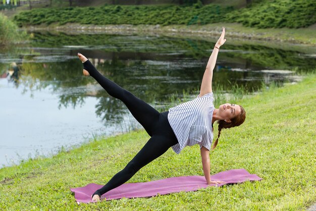 Mujer hermosa joven que hace ejercicio de yoga en el parque verde. Concepto de fitness y estilo de vida saludable.