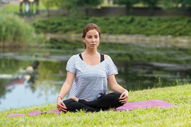 Foto gratuita mujer hermosa joven que hace ejercicio de yoga en el parque verde. concepto de fitness y estilo de vida saludable.