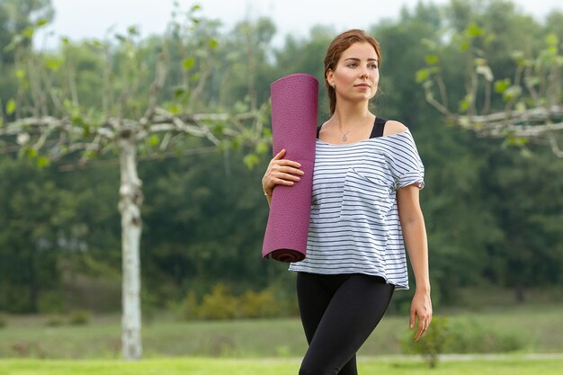 Mujer hermosa joven que hace ejercicio de yoga en el parque verde. Concepto de fitness y estilo de vida saludable.