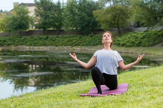 Mujer hermosa joven que hace ejercicio de yoga en el parque verde. Concepto de fitness y estilo de vida saludable.