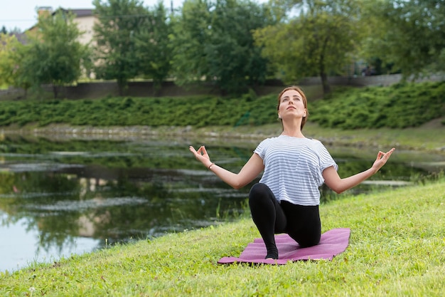 Mujer hermosa joven que hace ejercicio de yoga en el parque verde. Concepto de fitness y estilo de vida saludable.