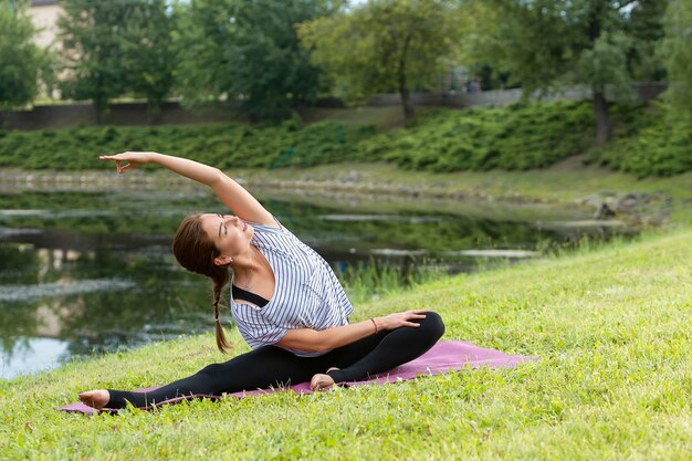 Mujer hermosa joven que hace ejercicio de yoga en el parque verde. Concepto de fitness y estilo de vida saludable.