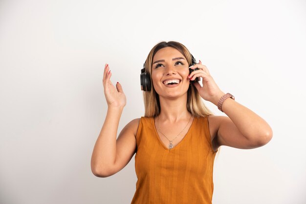 Mujer hermosa joven que lleva puestos los auriculares sobre el fondo blanco.