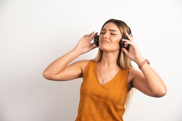 Mujer hermosa joven que lleva puestos los auriculares sobre el fondo blanco.