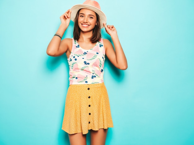 Foto gratuita mujer hermosa joven que mira la cámara en sombrero. chica de moda en verano casual camiseta blanca y falda amarilla en gafas de sol redondas. la hembra positiva muestra emociones faciales. modelo divertido aislado en azul