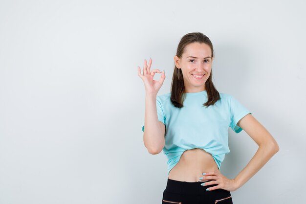 Mujer hermosa joven que muestra un gesto aceptable en camiseta y parece contento. vista frontal.