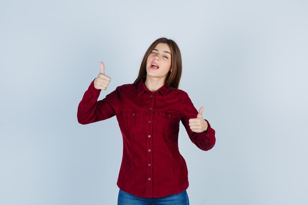 Mujer hermosa joven que muestra los pulgares para arriba en camisa y parece alegre.