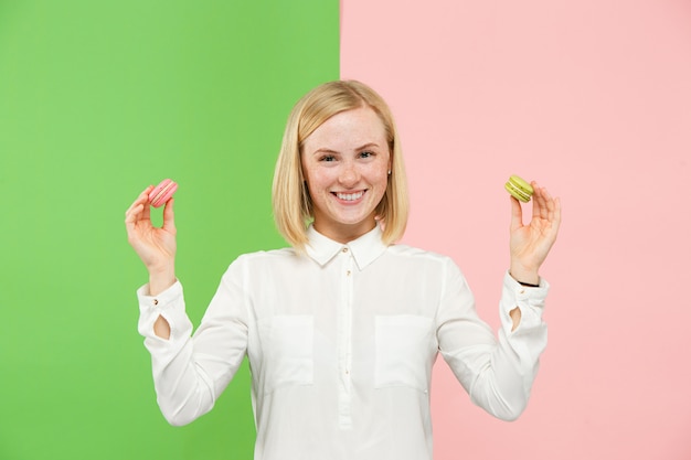 Mujer hermosa joven que sostiene los pasteles de los macarrones en sus manos, sobre coloreado de moda en el estudio.