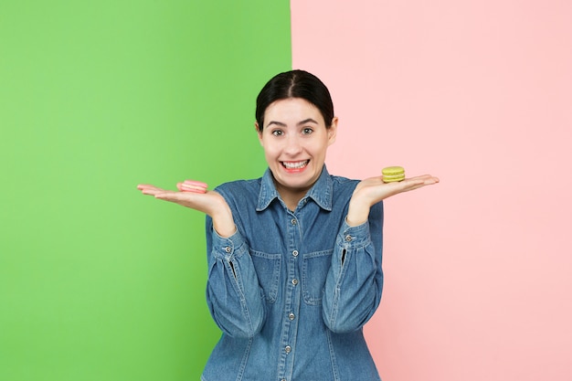 Mujer hermosa joven que sostiene los pasteles de los macarrones en sus manos