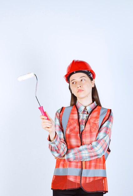 Mujer hermosa joven que sostiene el rodillo de pintura para pintar la reparación de la pared.