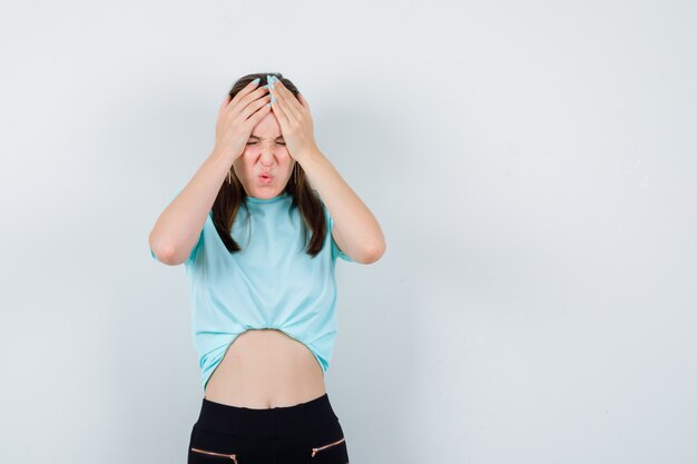 Mujer hermosa joven que sufre de dolor de cabeza en camiseta y luce dolorosa, vista frontal.