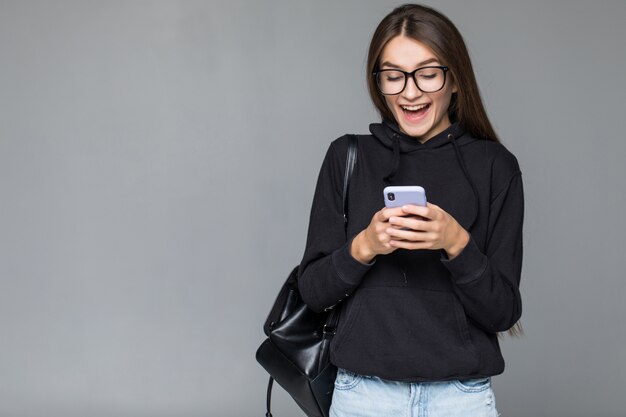 Mujer hermosa joven que usa el teléfono inteligente aislado en la pared gris